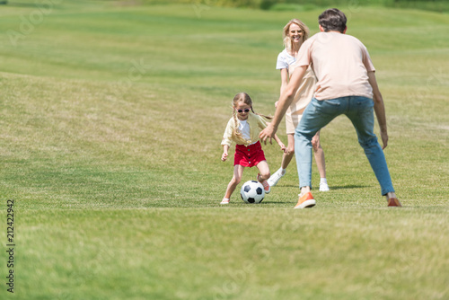 happy family with one child playing with soccer ball in park