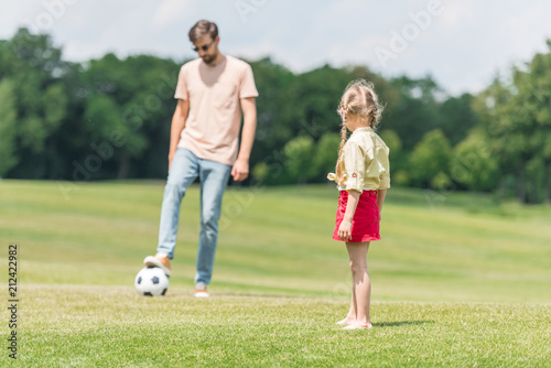 father and cute little daughter playing with soccer ball on lawn