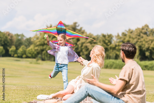 happy family with one child playing with colorful kite in park