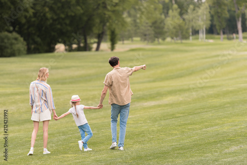 back view of family with one child holding hands and walking together in park