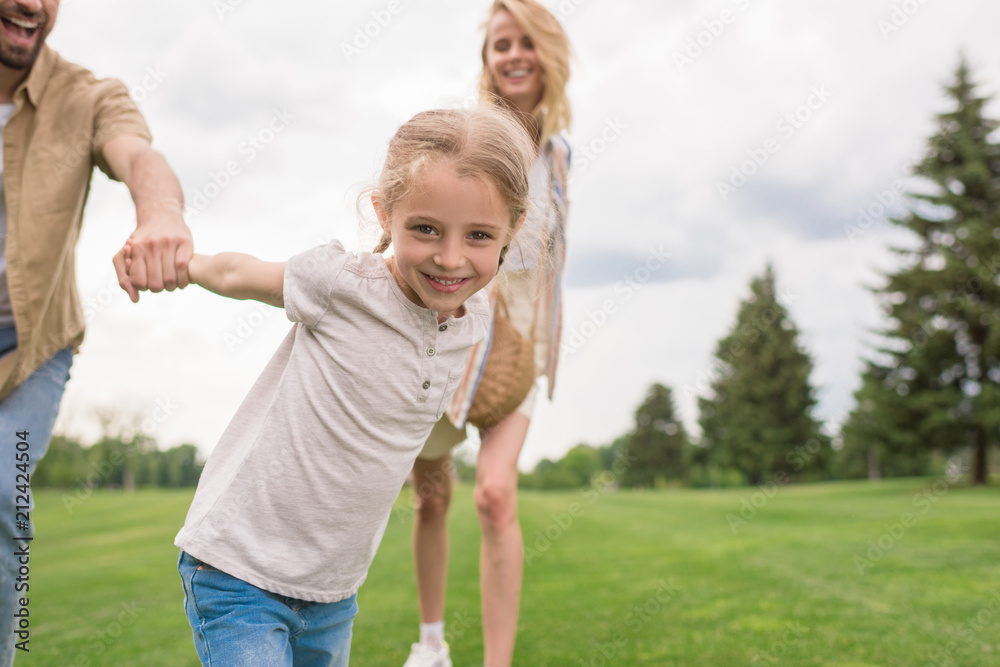 cropped shot of parents with daughter holding hands and child smiling at camera in park cropped shot of parents with daughter holding hands and child smiling at camera in park