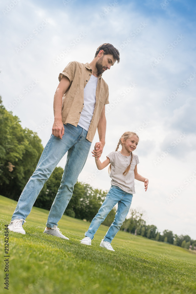 low angle view of father and little daughter holding hands while spending time together in park low angle view of father and little daughter holding hands while spending time together in park