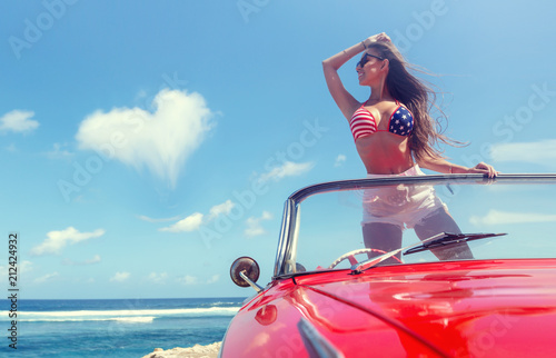 Happy woman in american patriotic bikini stay in retro car at the sunny beach