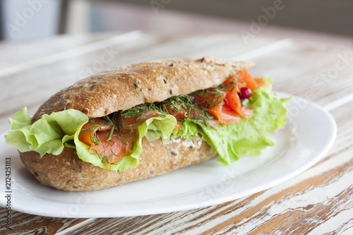 Аппетитный бутерброд с лососем и салатом на белой тарелке