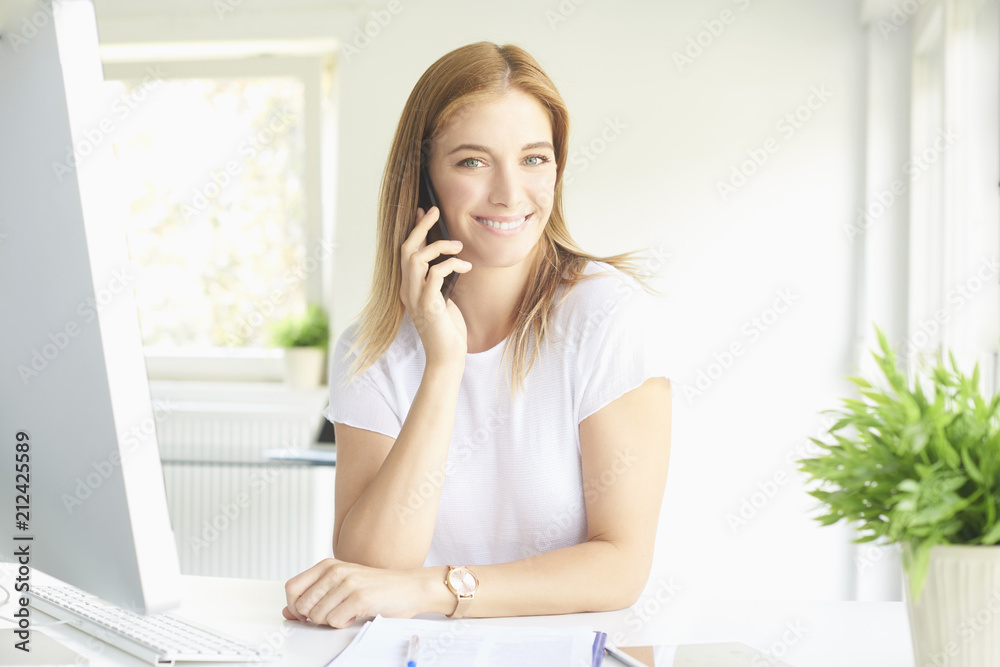 Happy woman at modern office. Portrait of beautiful happy young businesswoman looking at camera and laughing while talking somebody with her mobile phone. Happy woman at modern office. Portrait of beautiful happy young businesswoman looking at camera and laughing while talking somebody with her mobile phone.