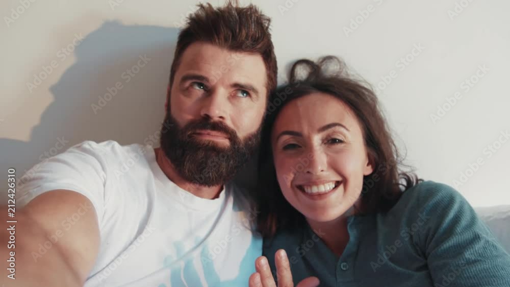 Smiling bearded man with his pretty young wife recording video for vlog while staying in bed, recommending, big thumb up, smiling. Modern lifestyle, being online, internet. Contemporary families. Smiling bearded man with his pretty young wife recording video for vlog while staying in bed, recommending, big thumb up, smiling. Modern lifestyle, being online, internet. Contemporary families.