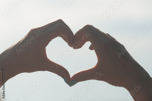 Female hands in the form of heart against the sky