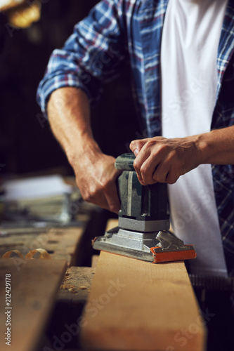 Carpenter using electric sander on wooden board in his workshop photo
