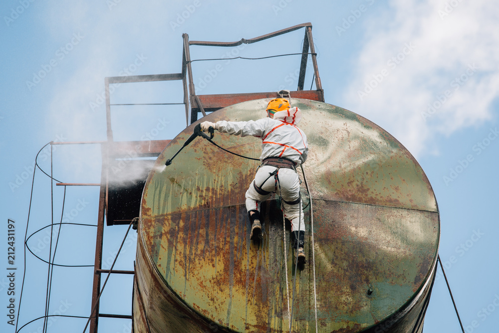 Industrial climber washing big barrel with water pressure. Risky job.