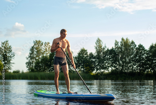 The guy is engaged in paddle boarding on the lake, © vulkanov