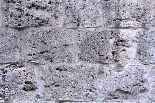 Texture - background of an old gray stone wall made of shellfish. The stone is all speckled with holes and scratches from time to time. There are streaks from seawater. Vintage old building