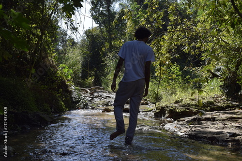 Pessoa a andar em corrente de água com rochas no interior de floresta tropical