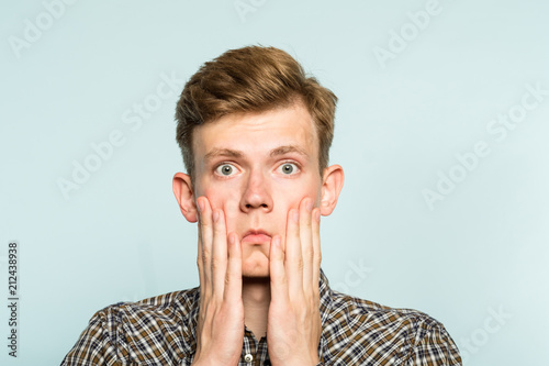 shocked speechless gobsmacked stunned man clutching his face. portrait of a young guy on light background. emotion facial expression. feelings and people reaction.