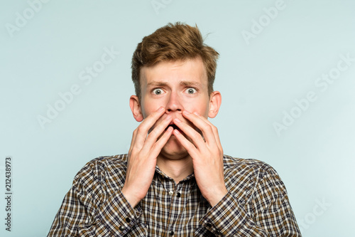scared shocked terrified frightened startled man clutching hands to his face. portrait of a young guy on light background. emotion facial expression. feelings and people reaction concept.