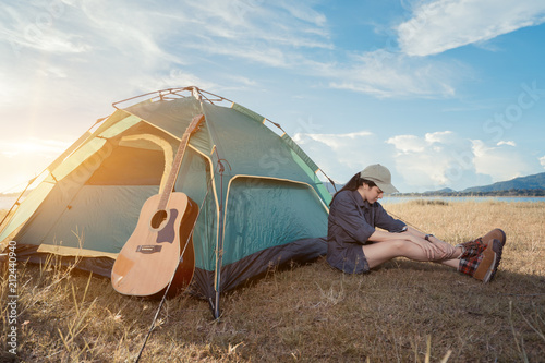 Asian woman camping and backpack travel sitting near tent relax alone with guitar at morning lifestyle nature mountain in forest.