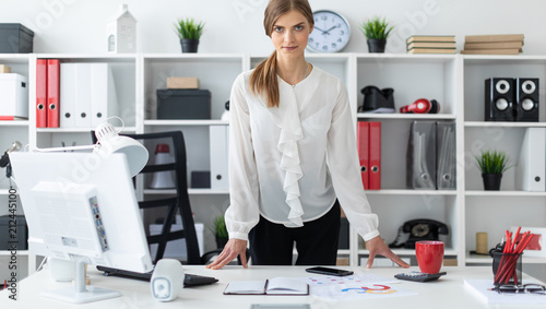 A young girl is standing right next to a table in the office. photo