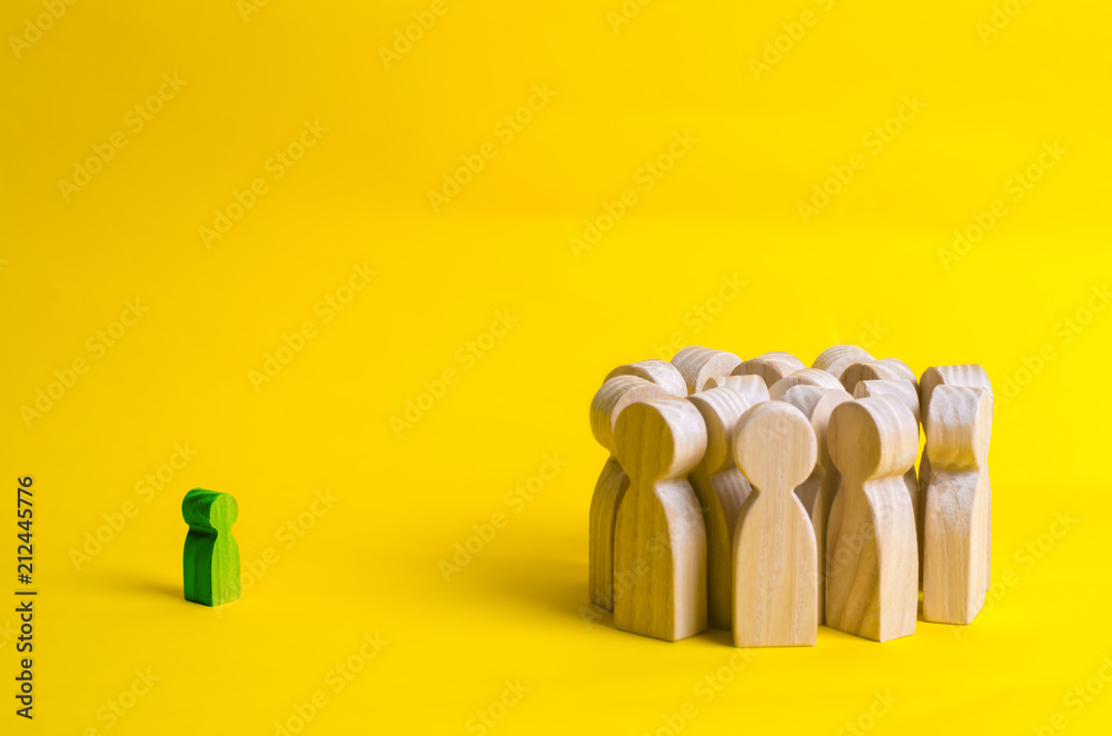 The crowd of wooden figures of people stand distantly and look at the little child. green figure of the child comes into contact with a group of adults. Adoption in the family, recognition by society.