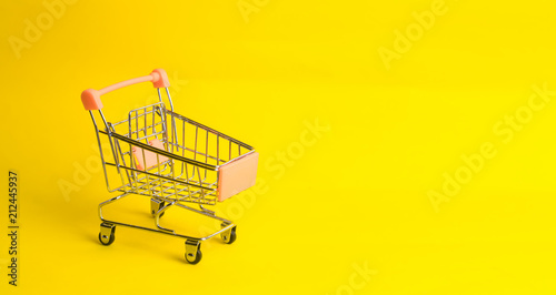 The supermarket cart stands on a yellow background. The concept of shopping and marketing, commerce and trade. The buying mood of people. Statistical data, trade balance.
