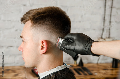 Barber does hair cut young guy on a brick wall background.