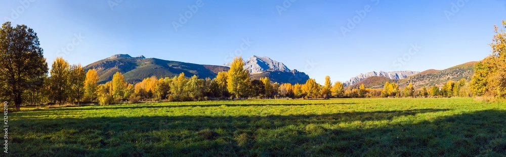 Vista panoramica de Paisaje  otoñal de prados verdes arboledas y montañas rocosas  al fondo. Con pequeño pueblo escondido entre los arboles