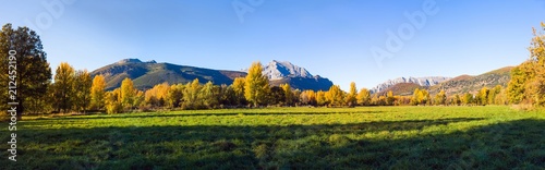 Vista panoramica de Paisaje  otoñal de prados verdes arboledas y montañas rocosas  al fondo. Con pequeño pueblo escondido entre los arboles photo