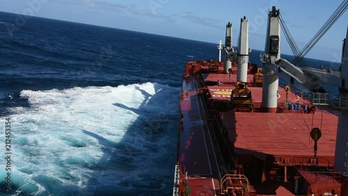 Cargo ship rolling in stormy sea. Huge waves under cloudless sky in South Atlantic.