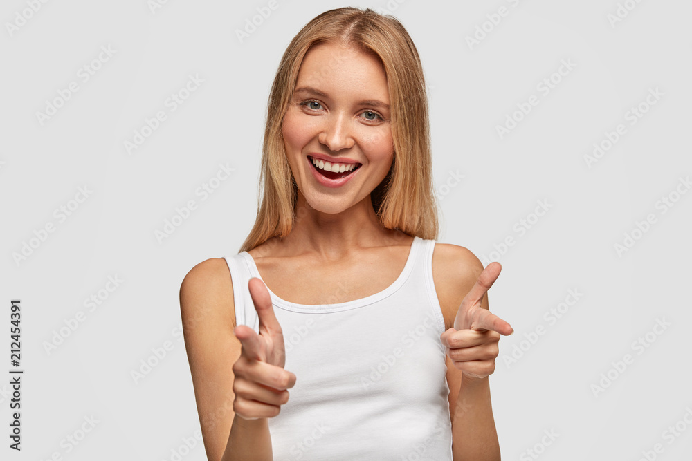 Portrait of happy cute blonde female with joyful expression, points at you with fore fingers directly at camera, chooses companions for entertainment, dressed casually, isolated over white background Portrait of happy cute blonde female with joyful expression, points at you with fore fingers directly at camera, chooses companions for entertainment, dressed casually, isolated over white background