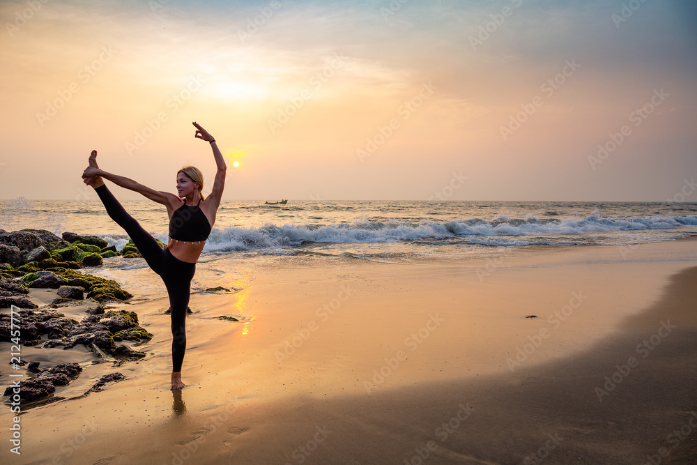 Fototapeta premium Middle age woman in black doing yoga on sand beach