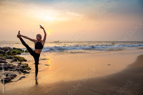 Middle age woman in black doing yoga on sand beach