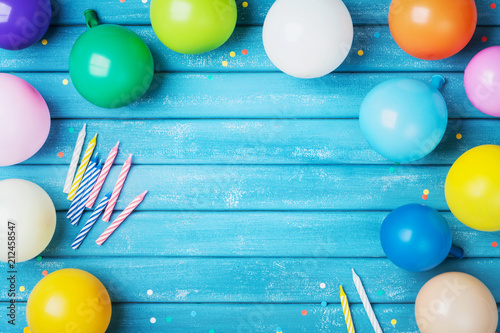 Heap of colorful balloons, confetti and candles on turquoise vintage table top view. Birthday party background. Festive greeting card.