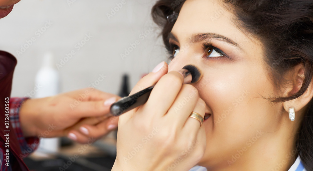 Master inflicts brush powder on the face of the girl, completes the day make-up in a beauty salon. Stylist at this time does a hairdo. Master inflicts brush powder on the face of the girl, completes the day make-up in a beauty salon. Stylist at this time does a hairdo.