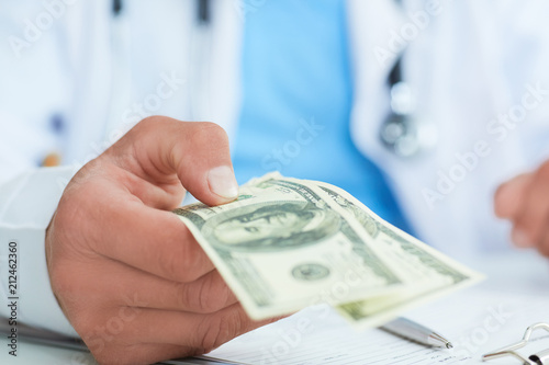 Male medicine doctor's hand holding two hundred dollars banknotes closae-up. Medic personnel salary, prestige and high paid job, education, public health business, medical insurance concept.