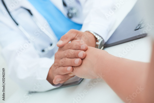 Hand of male doctor reassuring his female patient close-up. Medical ethics and trust concept.