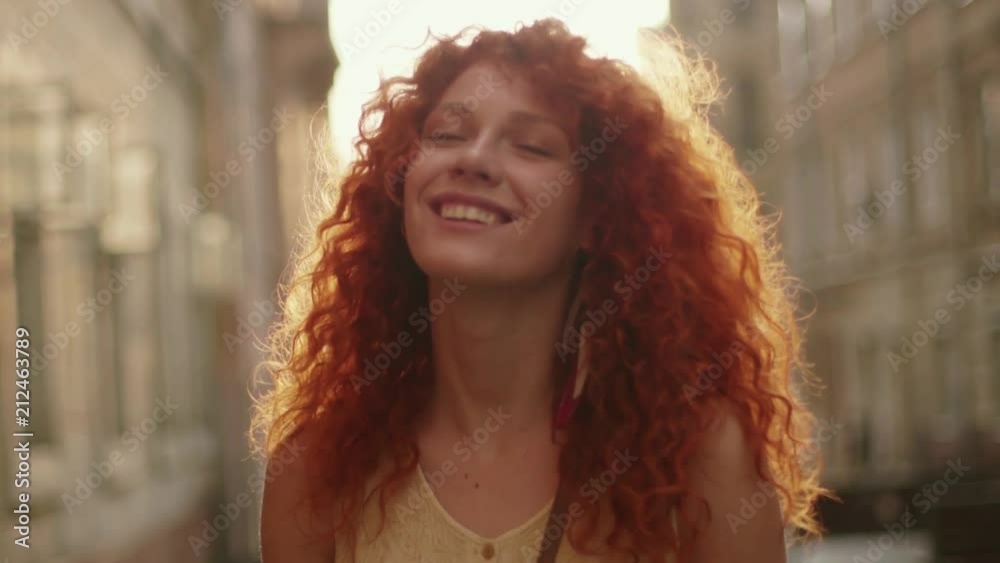 Sunshine young smiling woman with red curly hair look at camera smile walking in the city streets portrait happy slow motion summer face sunset beautiful lady outdoor closeup cute