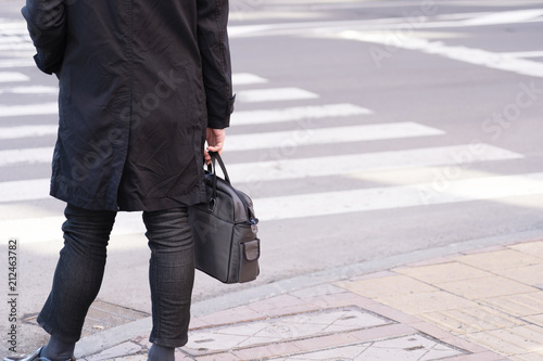 Businessman hang leather bag waiting for cross the road.