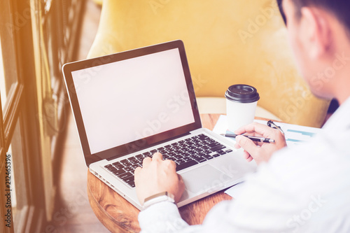 Business man hands holding pen and using laptop with blank screen on desk in cafe.