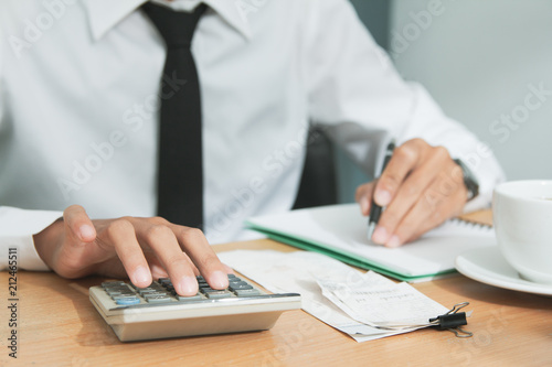 Asian man in white shirt holding pen writing a tax report lead to liquidation and using calculator on desk in office