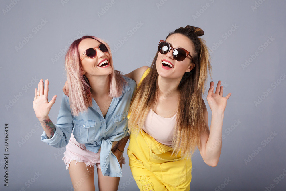 Carefree european woman in yellow denim overalls dancing with cheerful  caucasian friend in blue shirt. Indoor photo of two happy girls in summer  attires fooling around together. People, Friendship Stock Photo