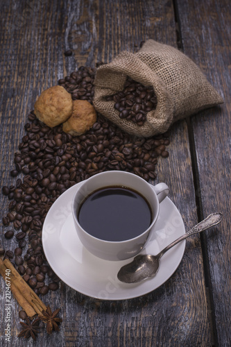Coffee in a cup, coffee beans, spice, cookies in the shape of heart on a wooden background.