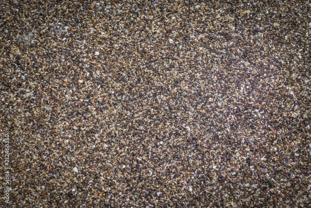 Texture of shallow coastal pebbles in water with reflection of sunlight shine, background with vignette Texture of shallow coastal pebbles in water with reflection of sunlight shine, background with vignette