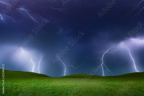 Powerful lightnings in dark stormy sky above green grass hills