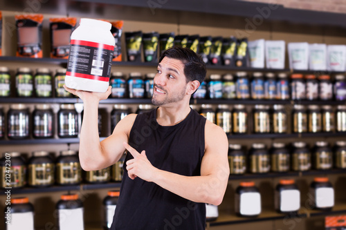 Positive athletic man seller  holding big pot of sport supplements i