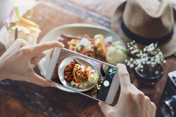 Young woman taking photo of food with smart phone in restaurant