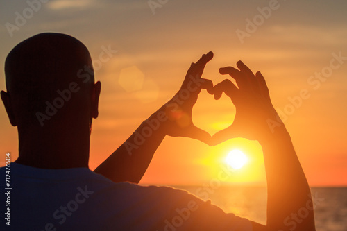 men's hands in the form of heart against sunlight in sunset sky, twilight time. Hands in shape of love heart, Love concept.