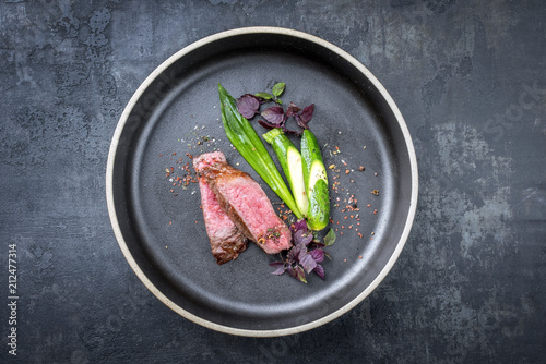 Modern barbecue dry aged sliced fillet steak with wild garlic and baby zucchini as top view on a plate with hot spices with copy space