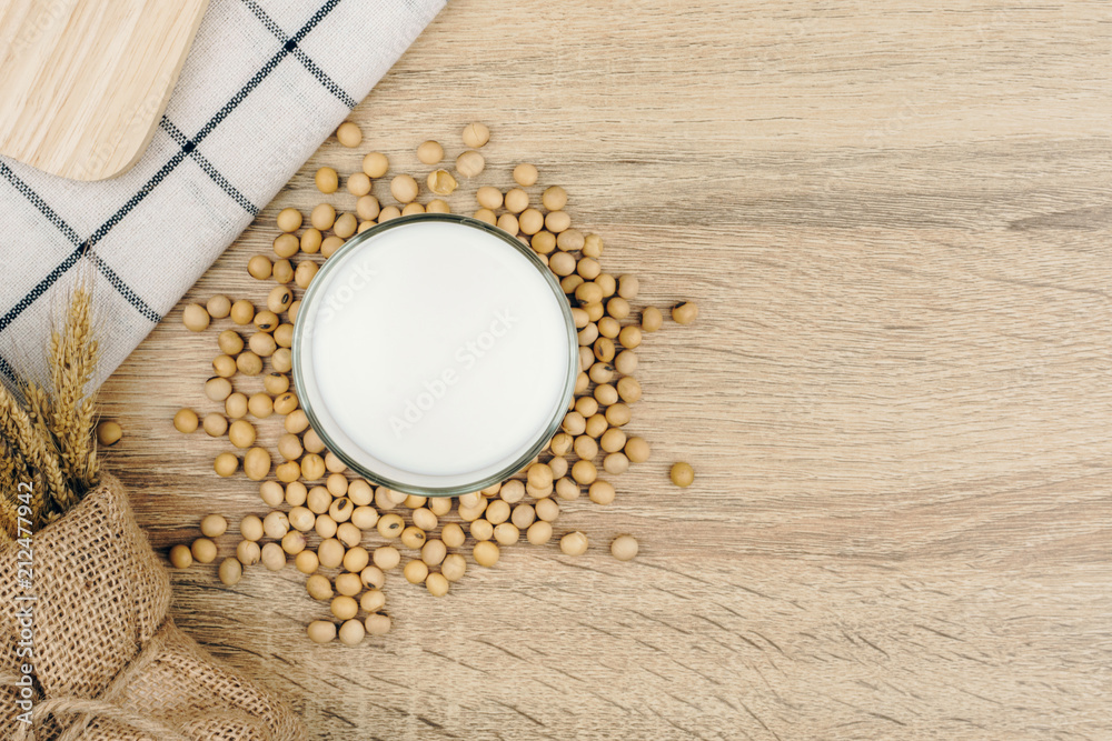 top view of a glass of soy milk, a pile of soybeans and dried wheat bouquet on the wooden table.