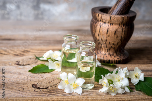 Essential jasmine oil with jasmine flowers and mortar on wooden background.