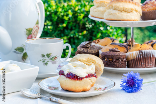 Afternoon tea with cakes and traditional English scones with strawberry jam and clotted cream set up on a table in the garden. Outdoor dining. photo