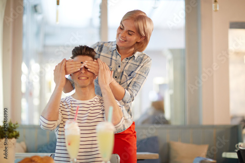 Happy girl covering her boyfriend eyes during their romantic date in cafe