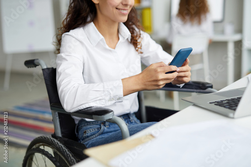 Businesswoman in white shirt and blue jeans messaging in smartphone by workplace